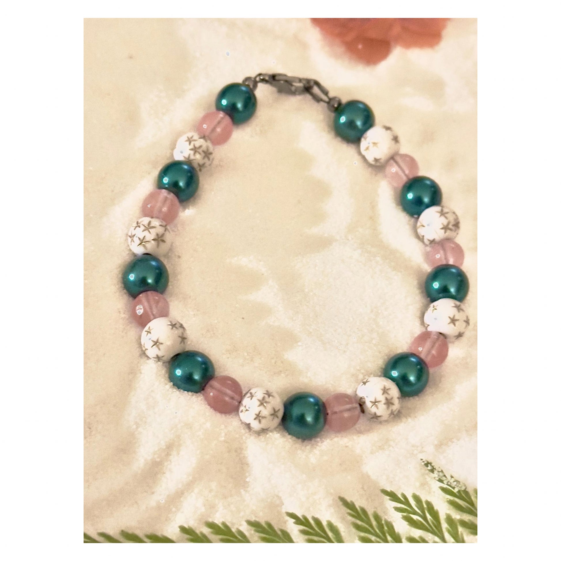 Handmade celestial bracelet with teal pearl beads, soft pink accents, and white star-pattern beads displayed on a neutral background