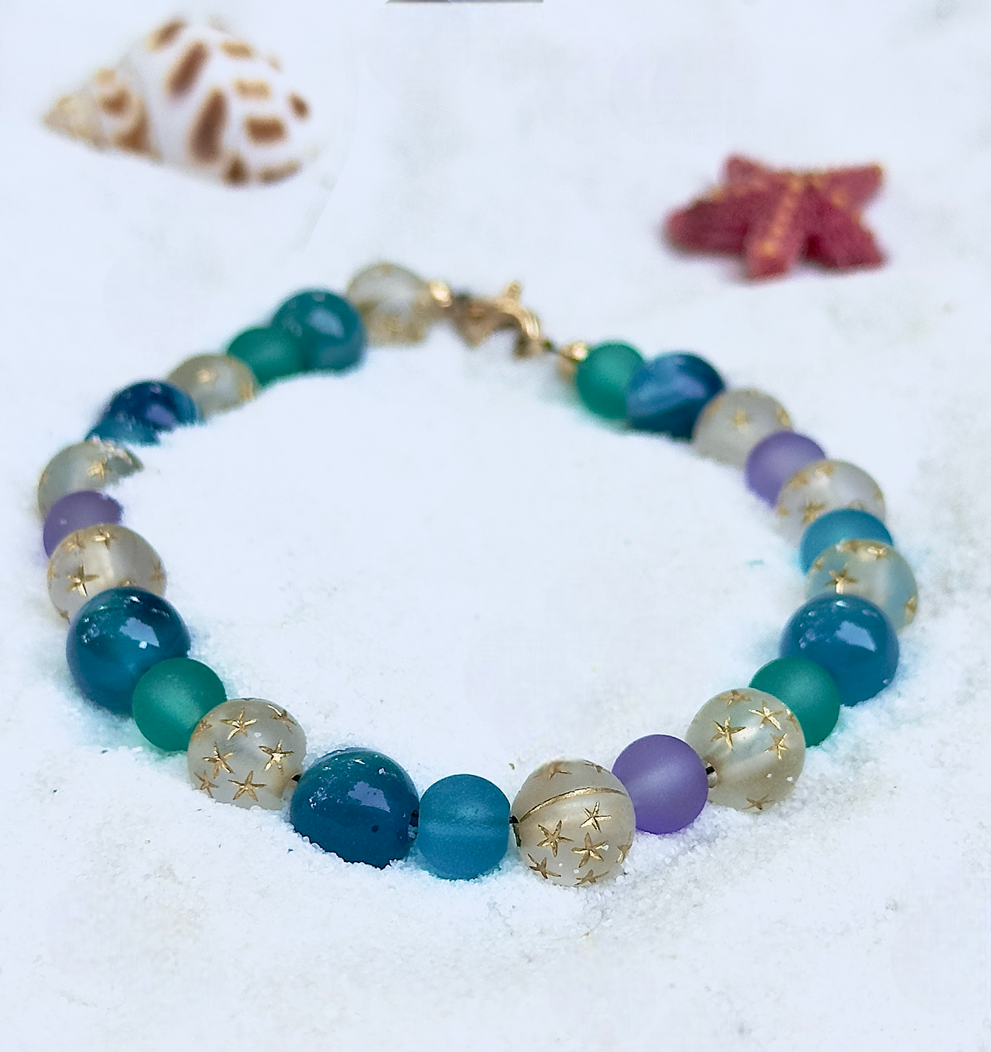 Multicolored beaded bracelet on a sandy surface with starfish and shell decorations.