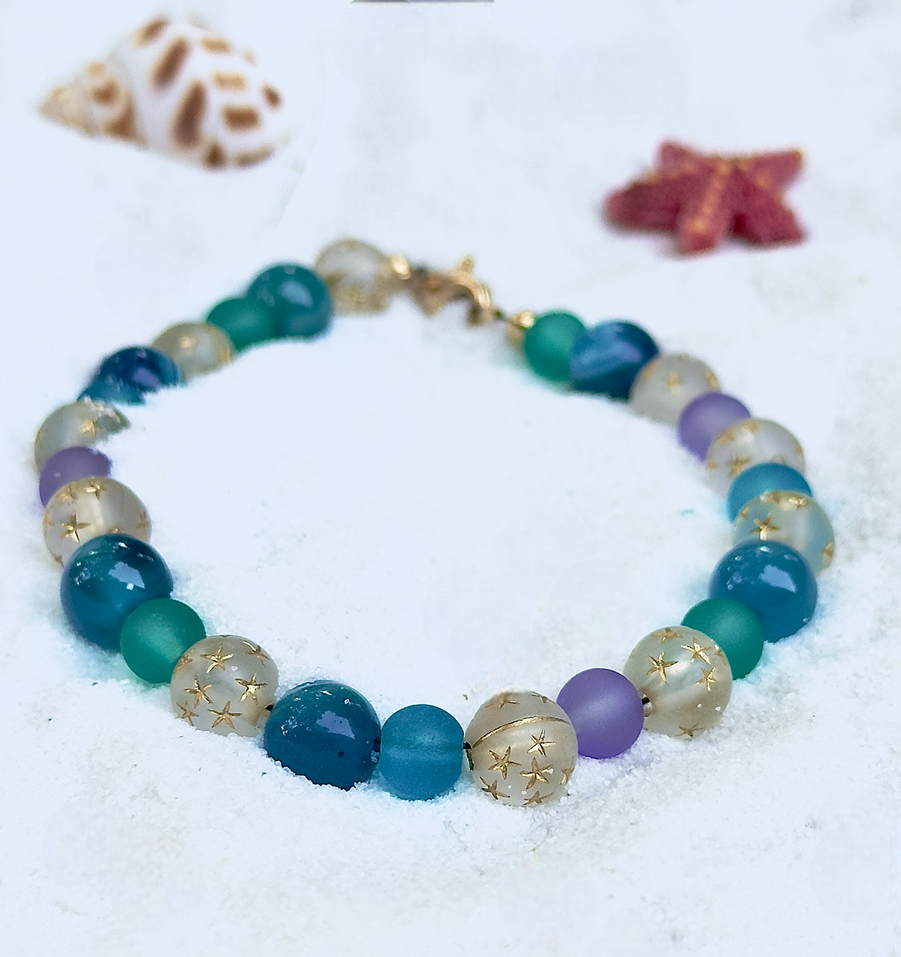 Multicolored beaded bracelet on a sandy surface with starfish and shell decorations.