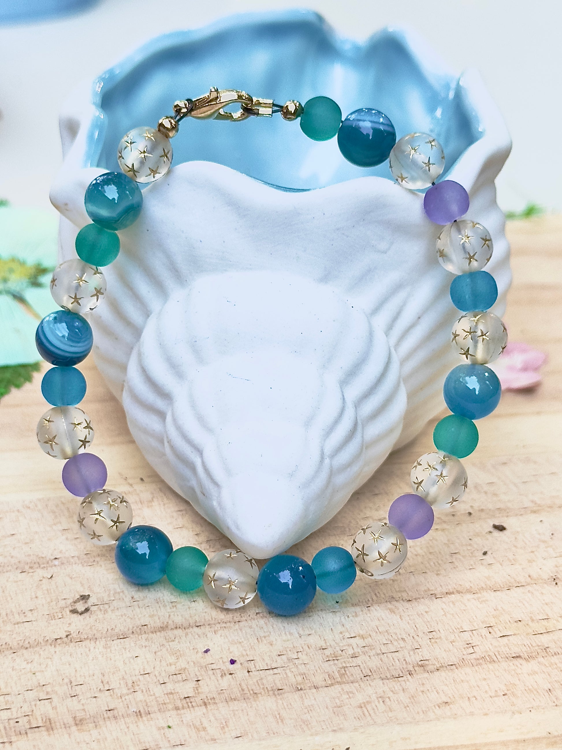 Celestial Opalite Sky bracelet with blue, teal, purple, and opalite beads displayed on a white shell against a light wood background

