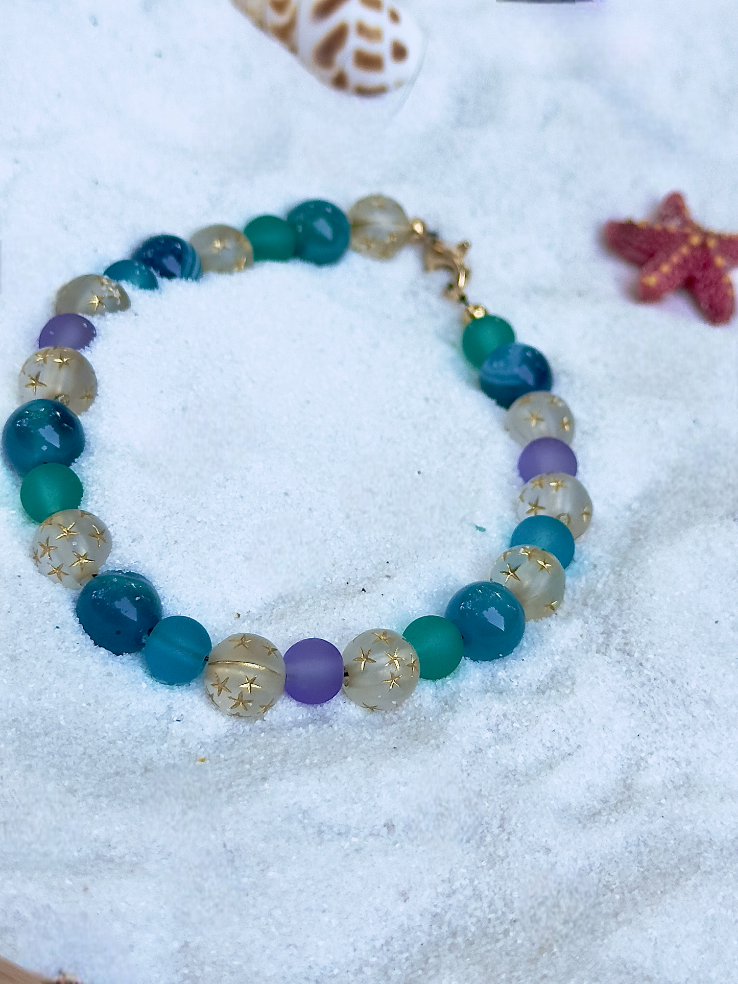 Multicolored beaded bracelet on a sandy surface with shells and starfish.