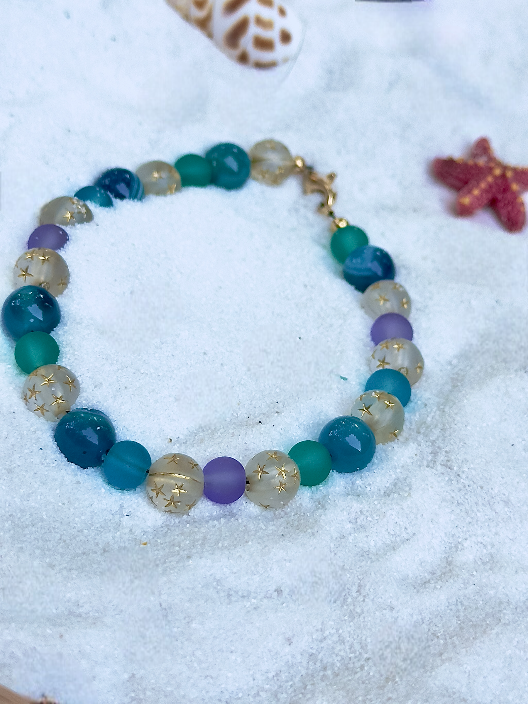 Multicolored beaded bracelet on a sandy surface with shells and starfish.