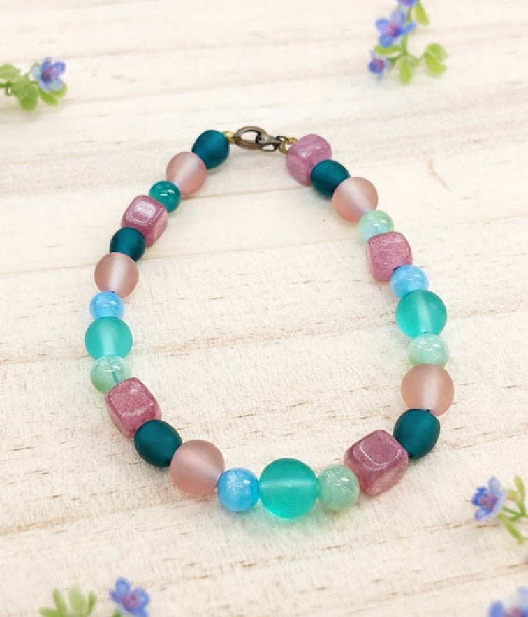 spring pastel gemstone bracelet styled with small flowers on light wood background coastal garden jewelry