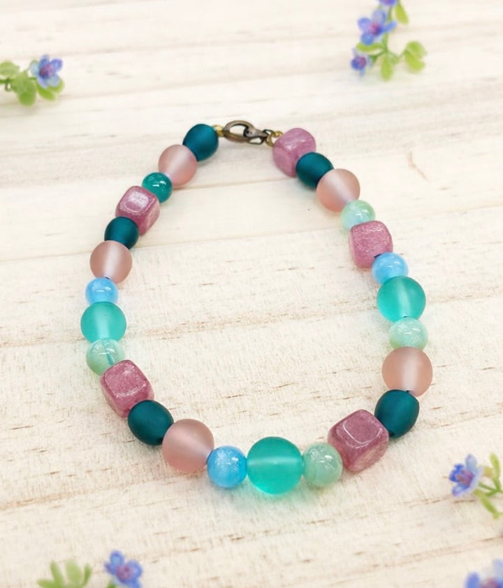 spring pastel gemstone bracelet styled with small flowers on light wood background coastal garden jewelry