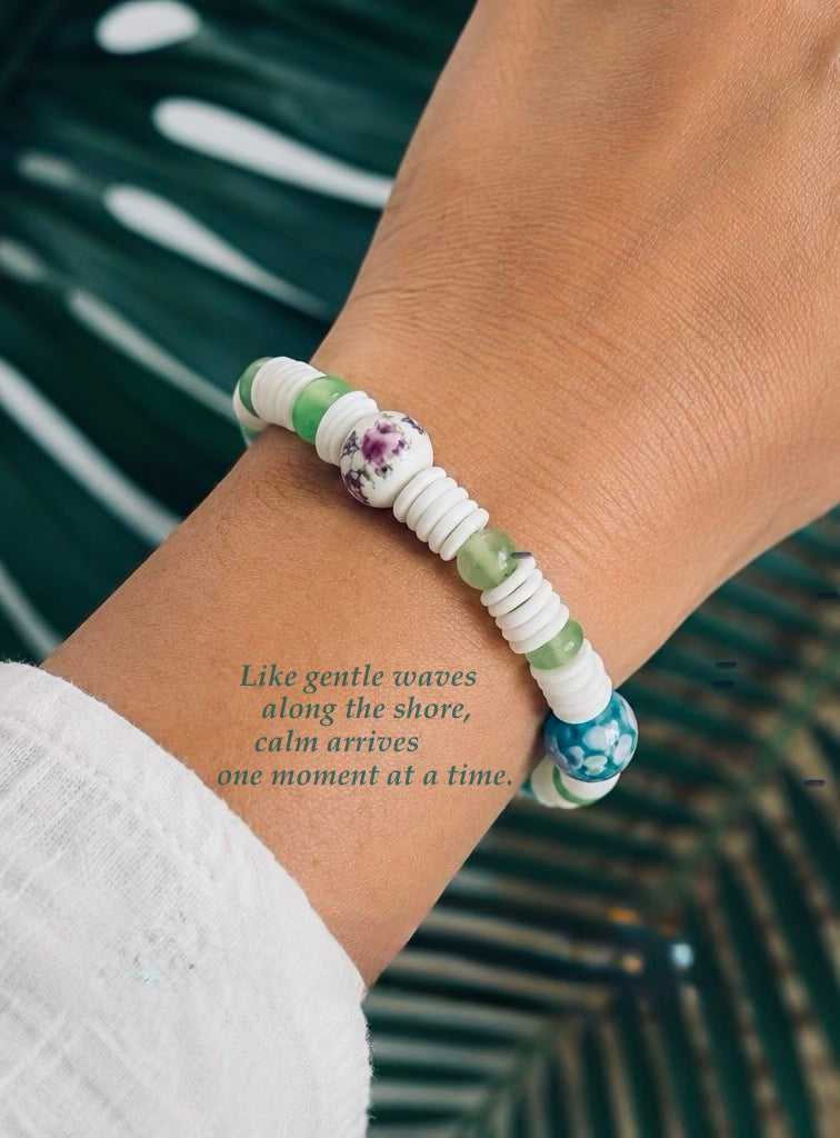 Person wearing Coastline Oasis bracelet with white heishi beads, green accents, and floral beads.