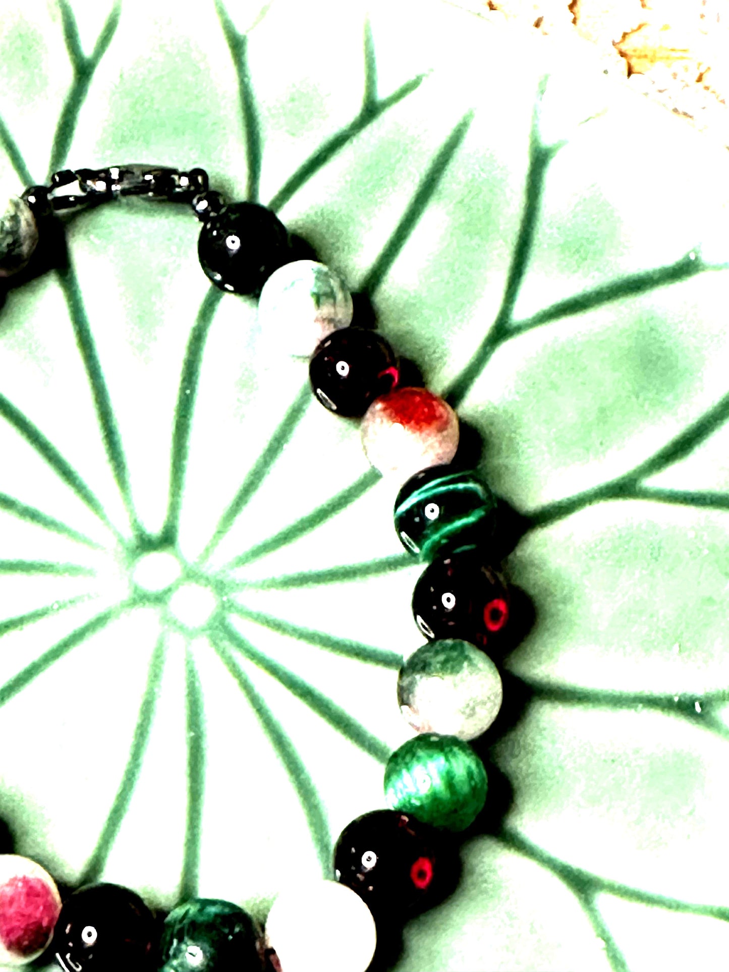 Partial view of festive gemstone bracelet focusing on bead colors and craftsmanship, photographed on a green ceramic background.