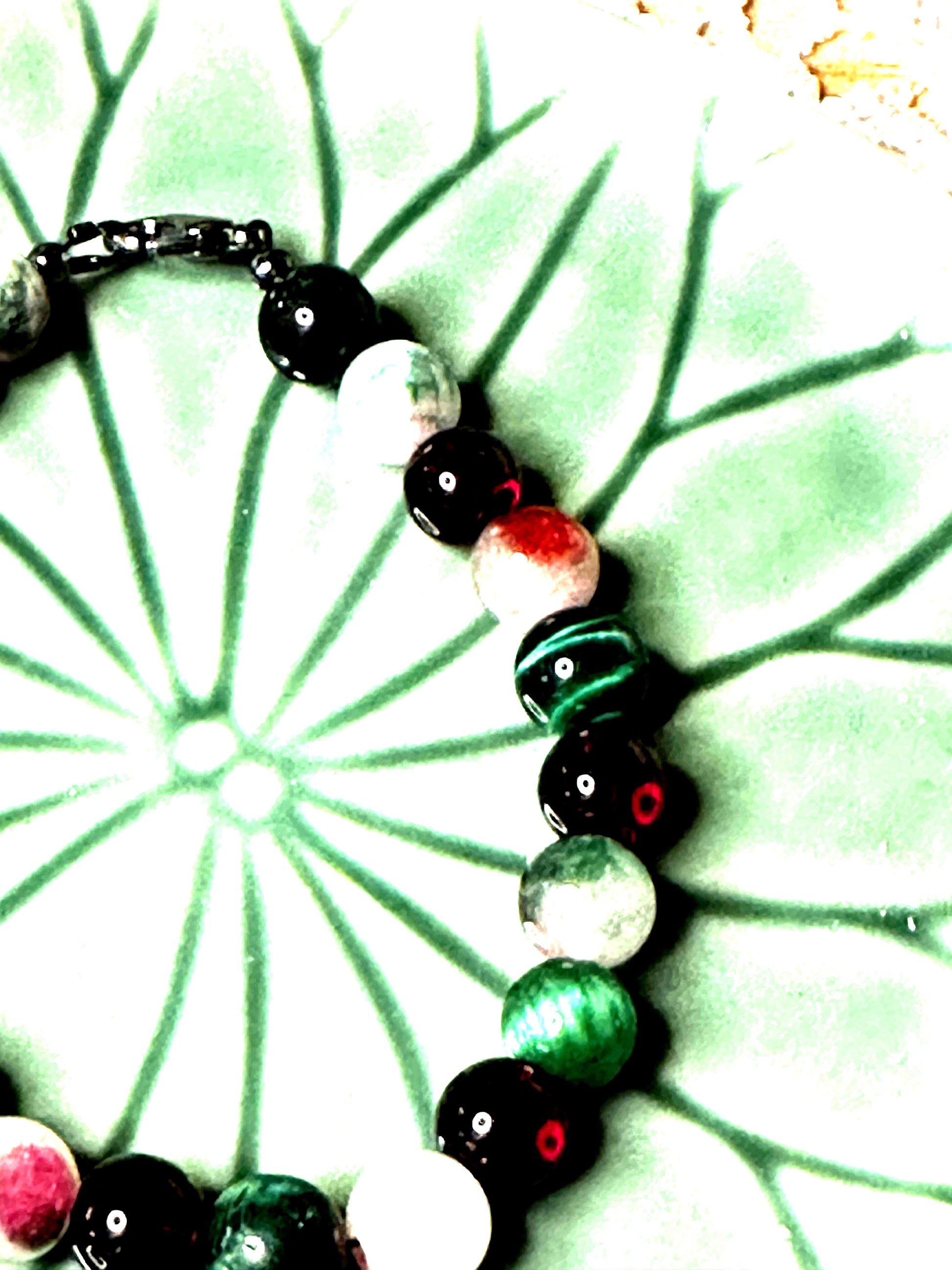 Partial view of festive gemstone bracelet focusing on bead colors and craftsmanship, photographed on a green ceramic background.