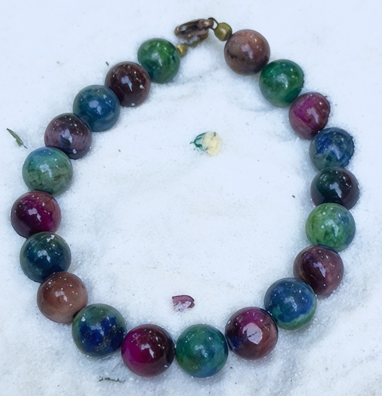 Multicolor beaded bracelet photographed on soft white sand background with gemstone accents