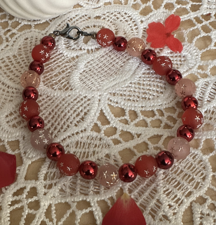     Whimsical cosmic bracelet featuring sparkle beads and crackle glass displayed with soft red heart accents on lace fabric