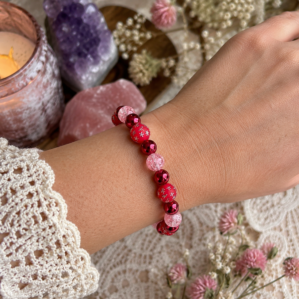     Lifestyle photo of red and pink celestial bracelet worn on wrist with crystals, candle, and soft floral accents