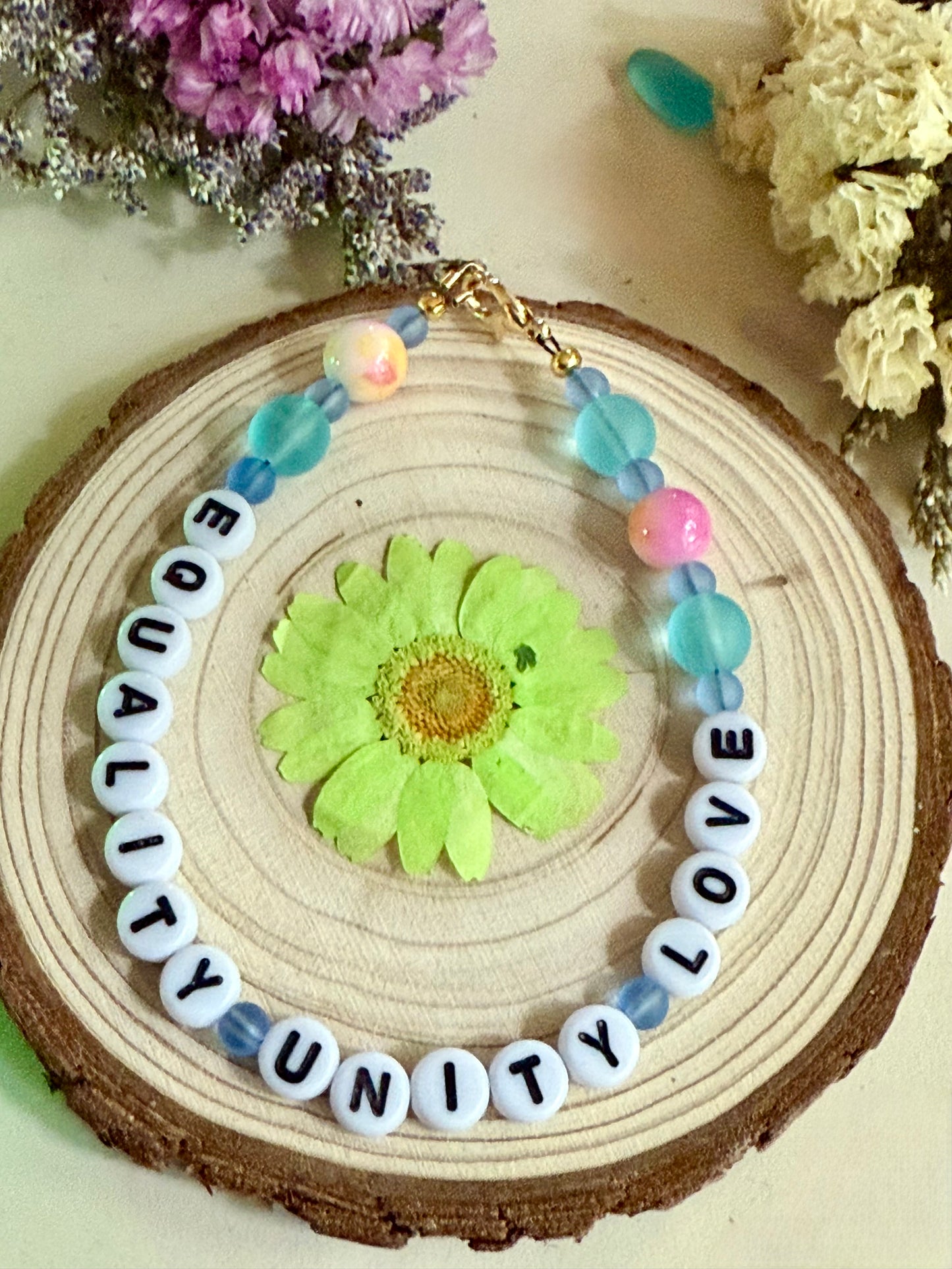 Equality Unity Love bracelet displayed on wood slice with floral accent colorful handmade bracelet