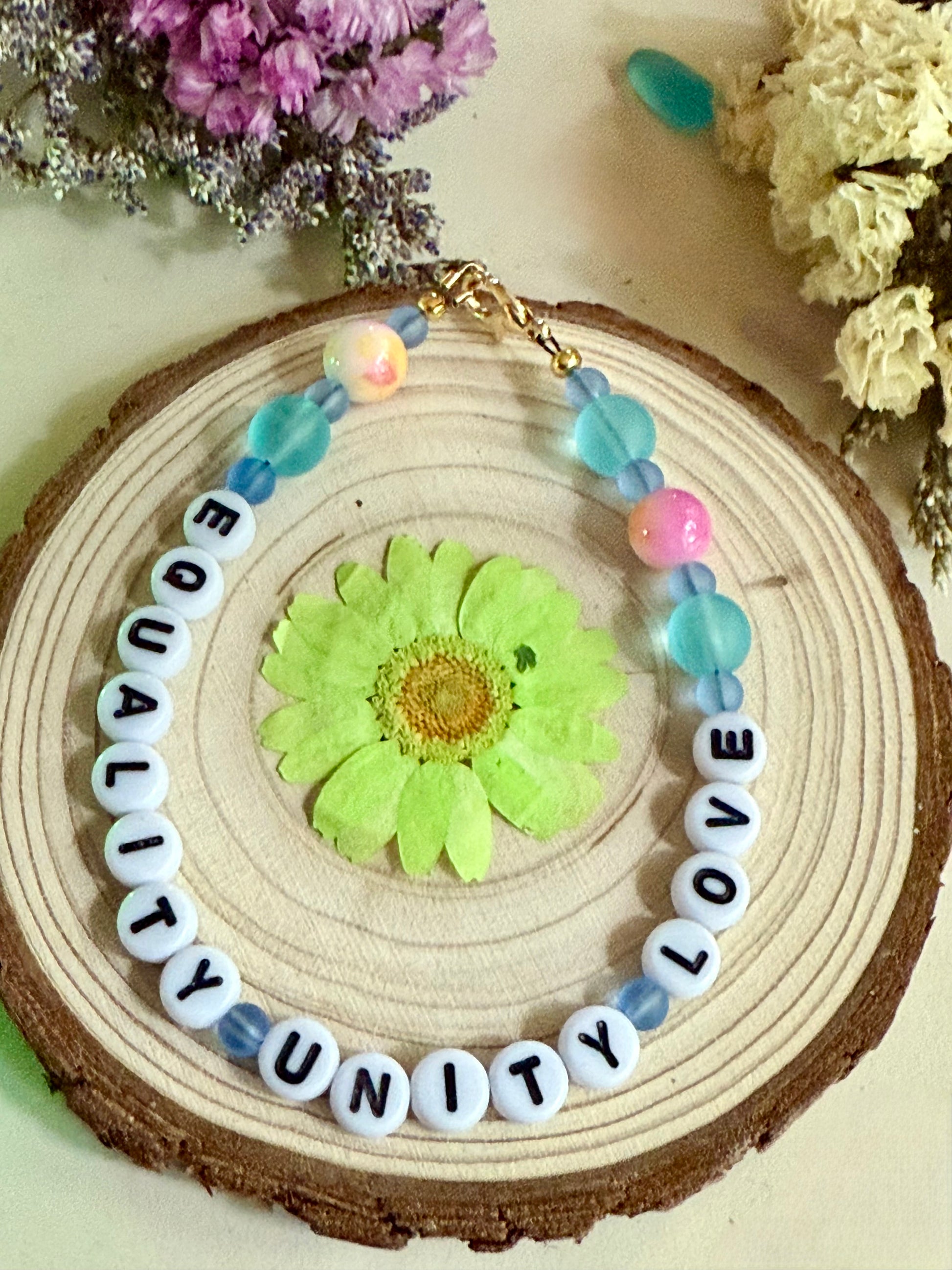 Equality Unity Love bracelet displayed on wood slice with floral accent colorful handmade bracelet
