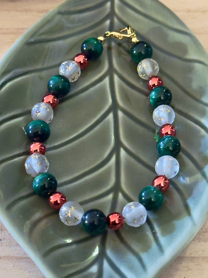 Deep green, frosted white star and rose-gold beaded bracelet displayed on a ceramic leaf tray.