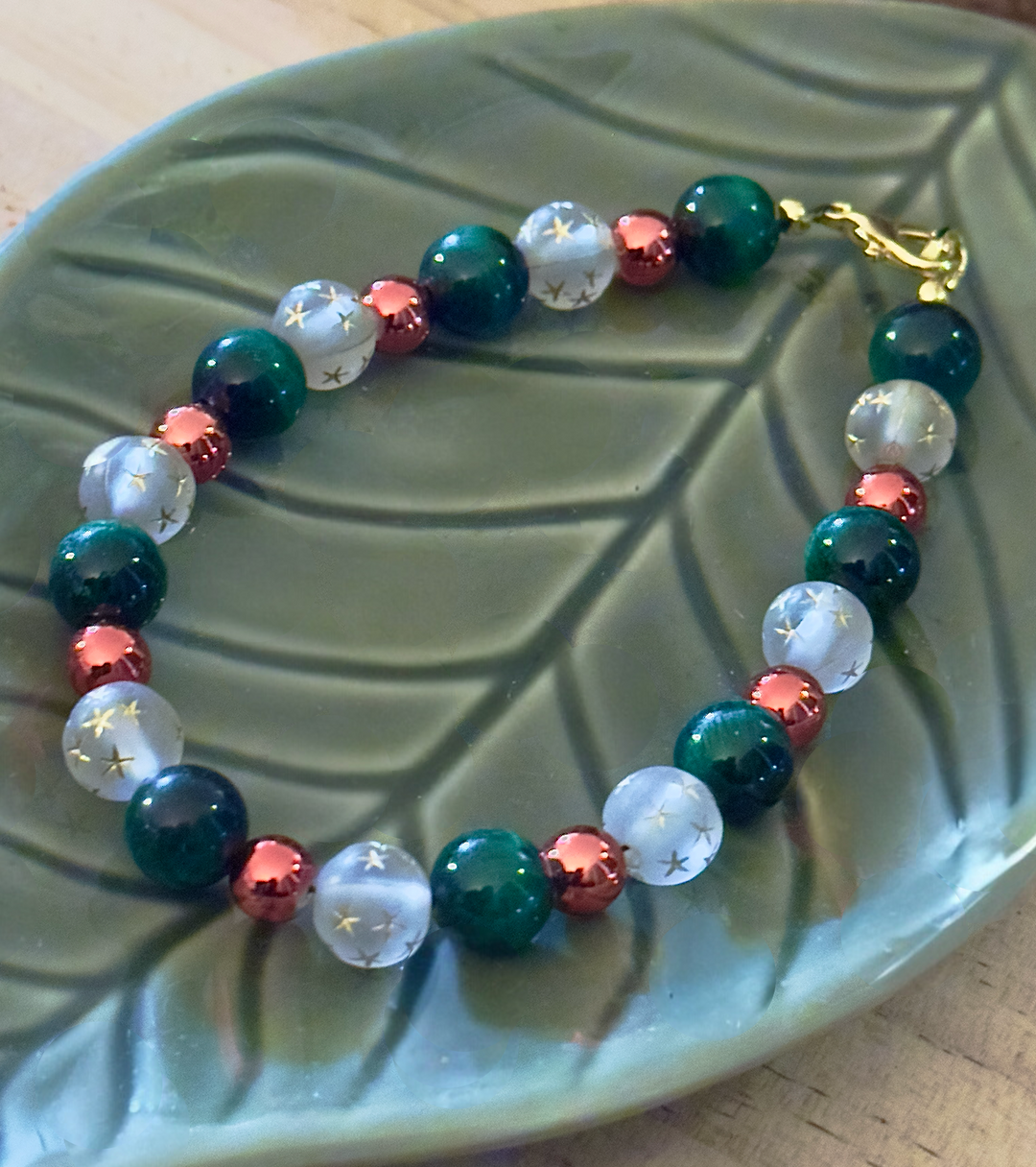 Full view of a deep green, frosted white and rose-gold bracelet arranged diagonally on a green ceramic leaf.