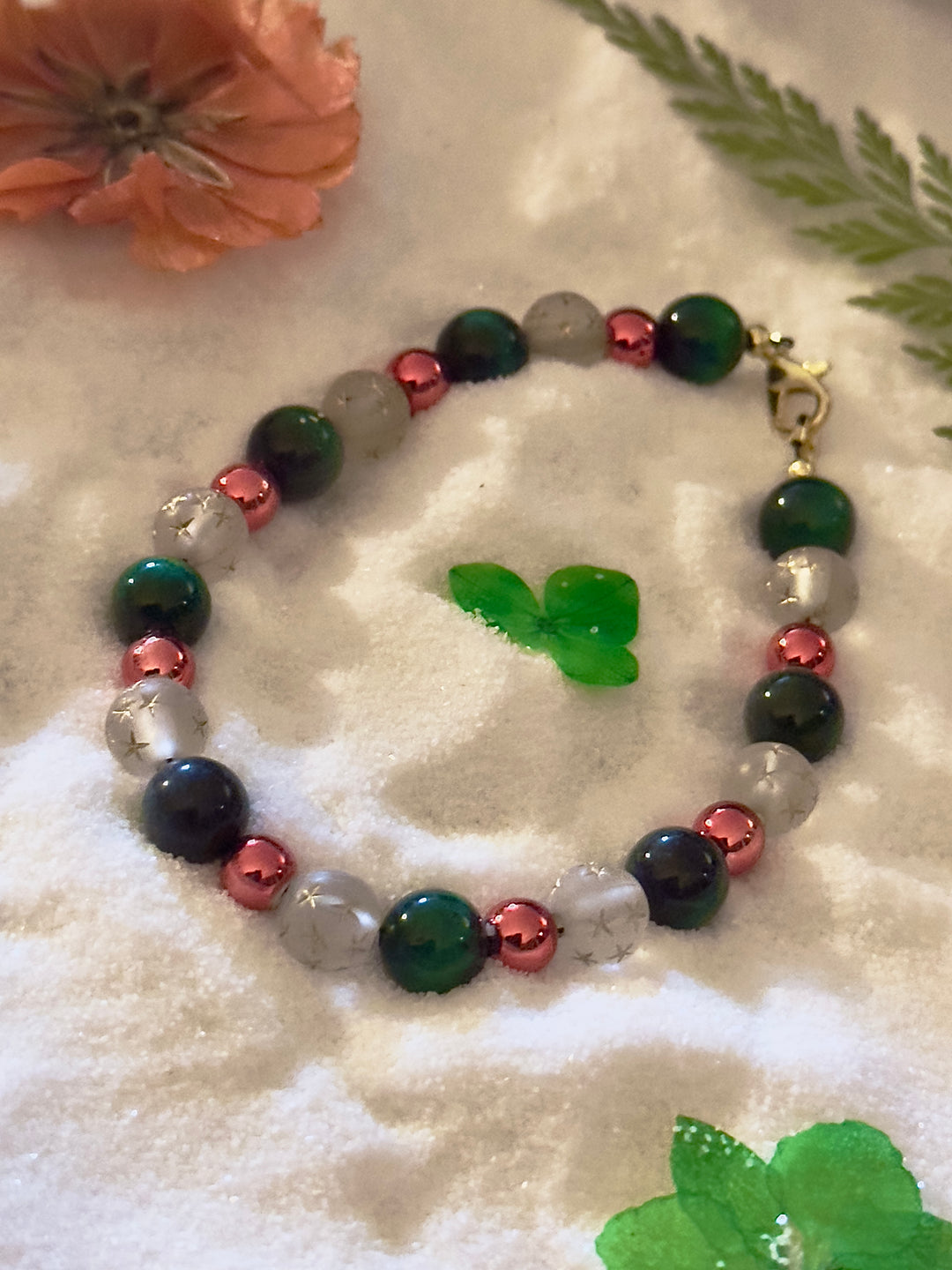 Angled close-up of a green and frosted white star bead bracelet with rose-gold accents and a gold clasp.