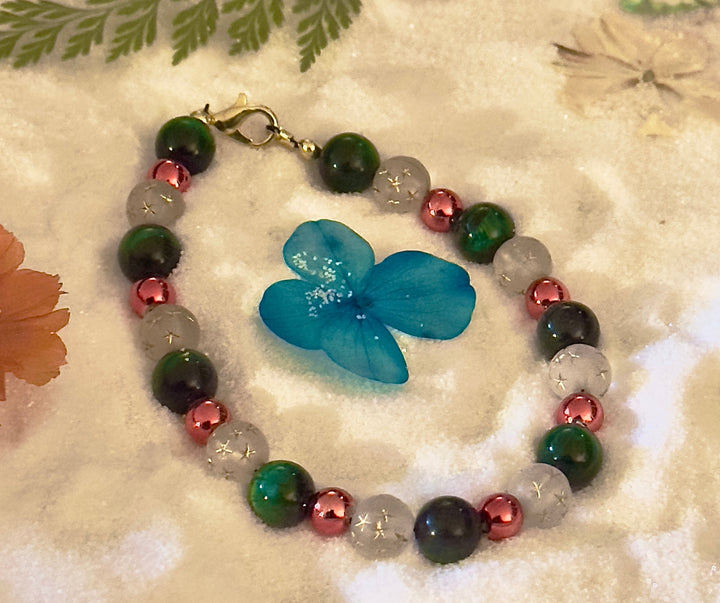 Green, white and rose-gold beaded bracelet styled on a soft sand background with a small green botanical accent.
