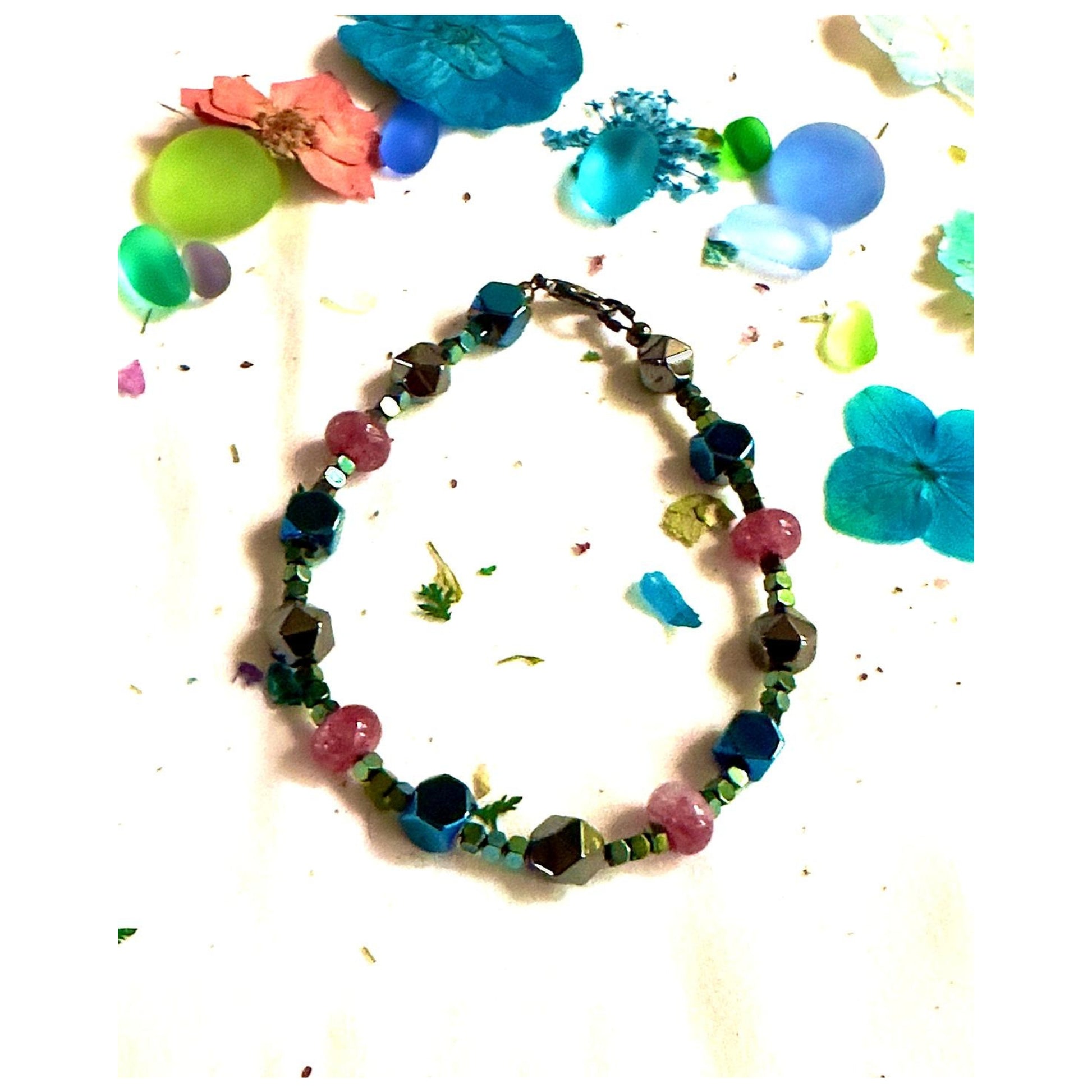 Afterglow gemstone bracelet arranged in a circular flat lay on a white background with colorful dried flowers and petals.
