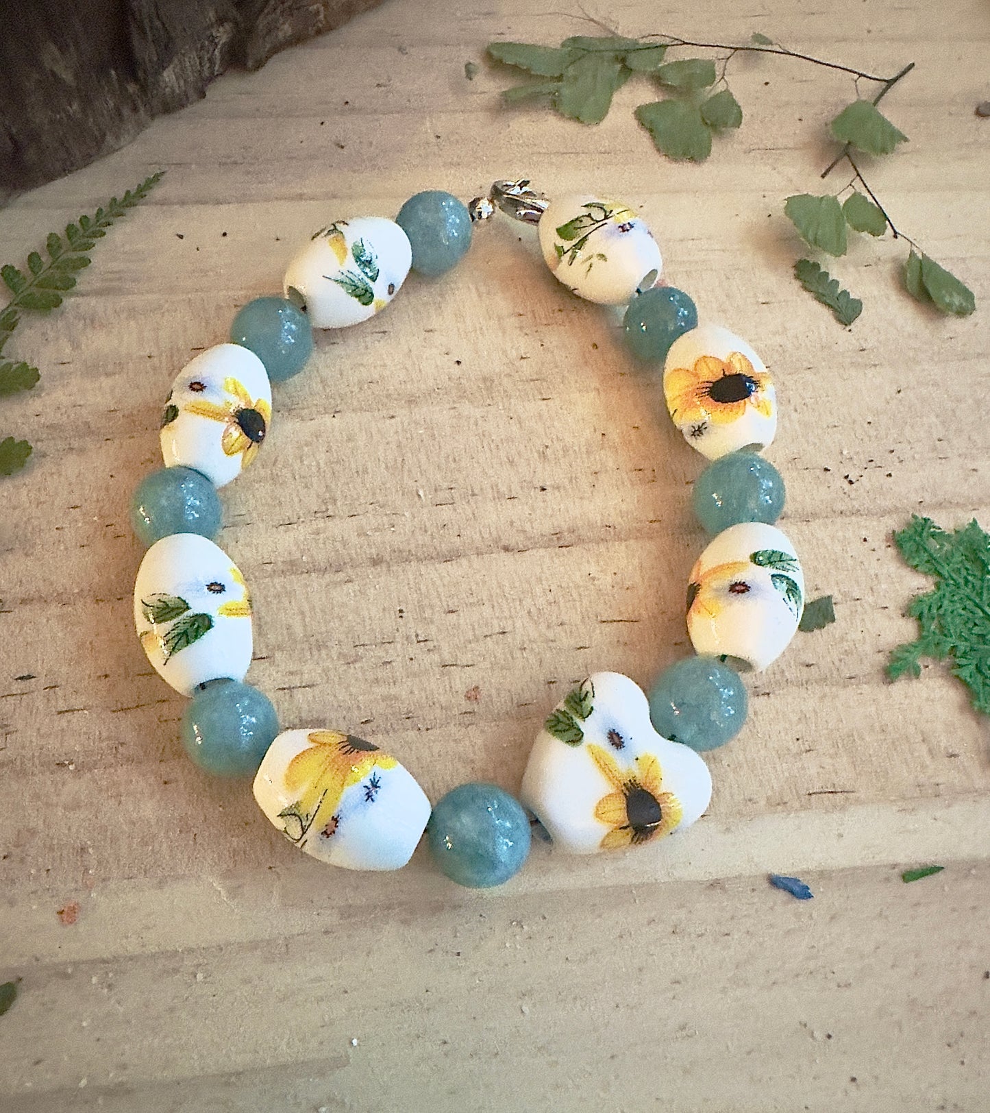 Circular sunflower bead bracelet with teal gemstones on rustic wooden surface
