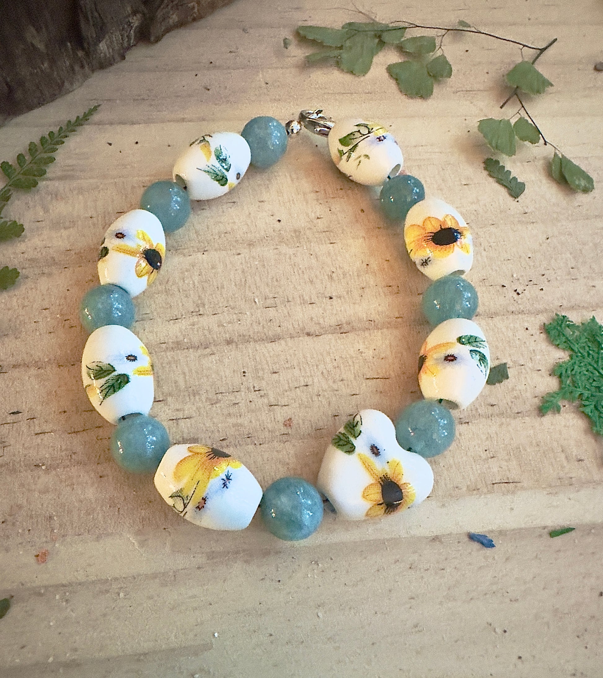 Circular sunflower bead bracelet with teal gemstones on rustic wooden surface