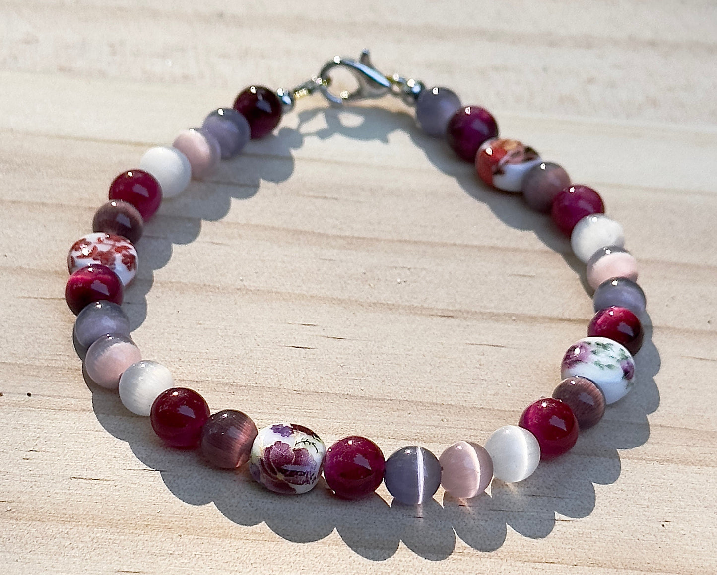     Fearlessly Crimson lesbian pride bracelet styled on a wooden background with flowers, seashells, candle, and affirmation cards.