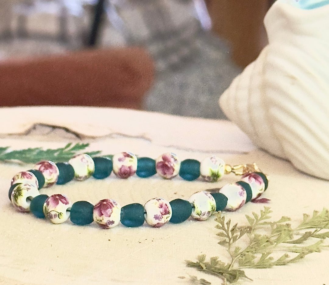 Handmade rose garden bracelet with teal matte beads and floral ceramic seashell decor on wood background