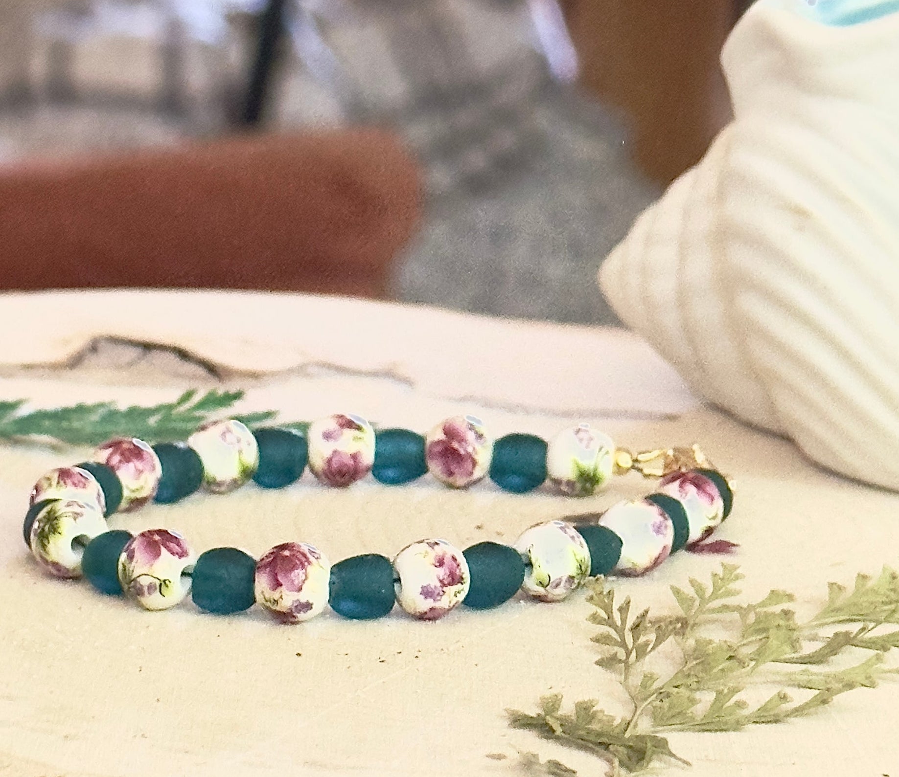 Handmade rose garden bracelet with teal matte beads and floral ceramic seashell decor on wood background