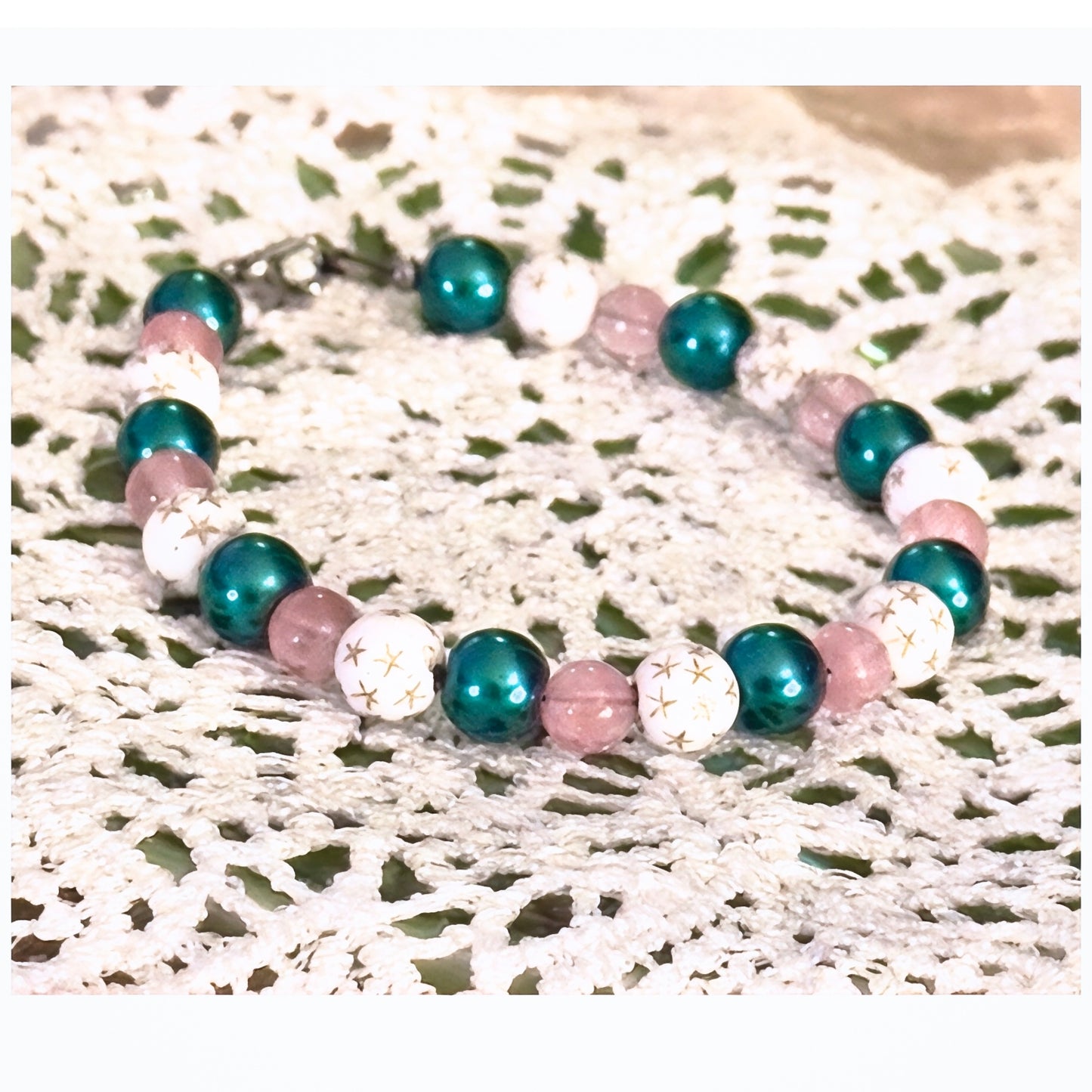 Pink teal galaxy beaded bracelet with star beads on lace background close-up
