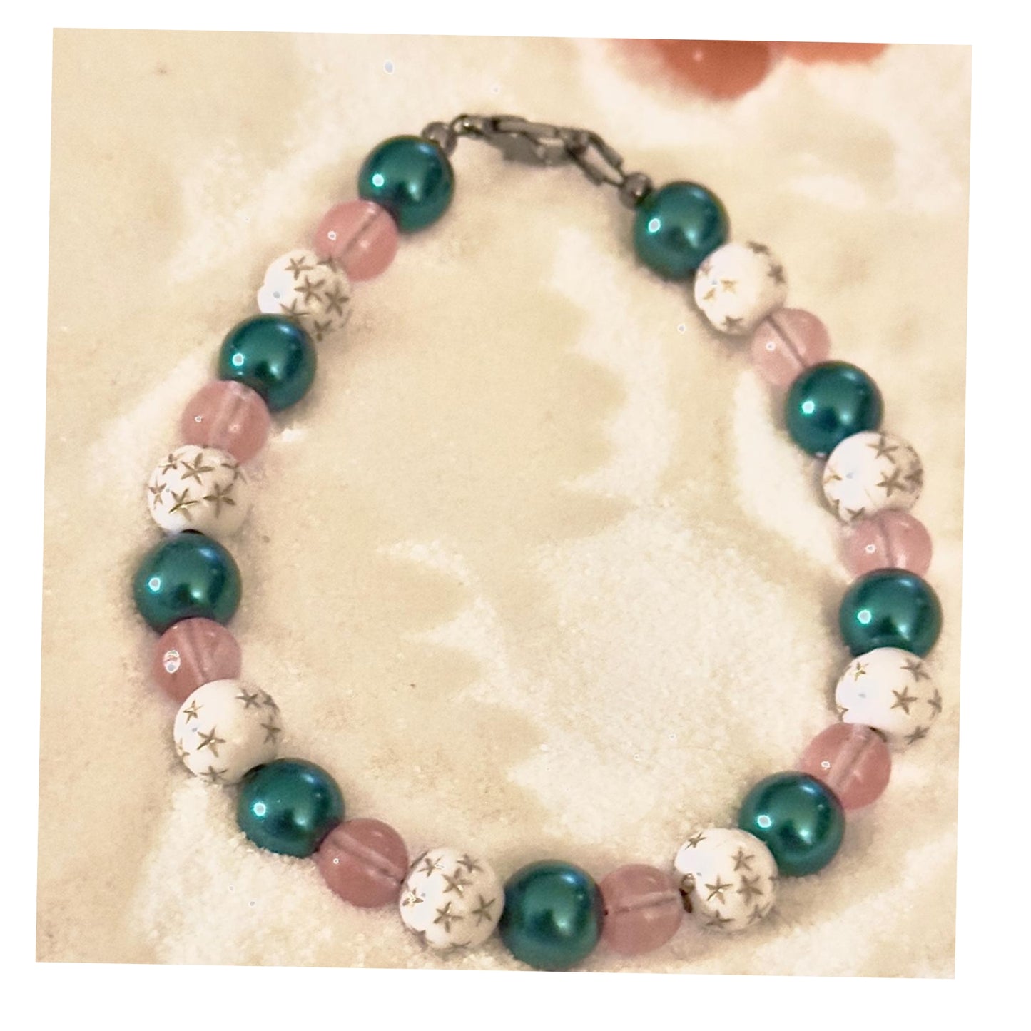 Handmade pink teal beaded bracelet with star accents on neutral sand background