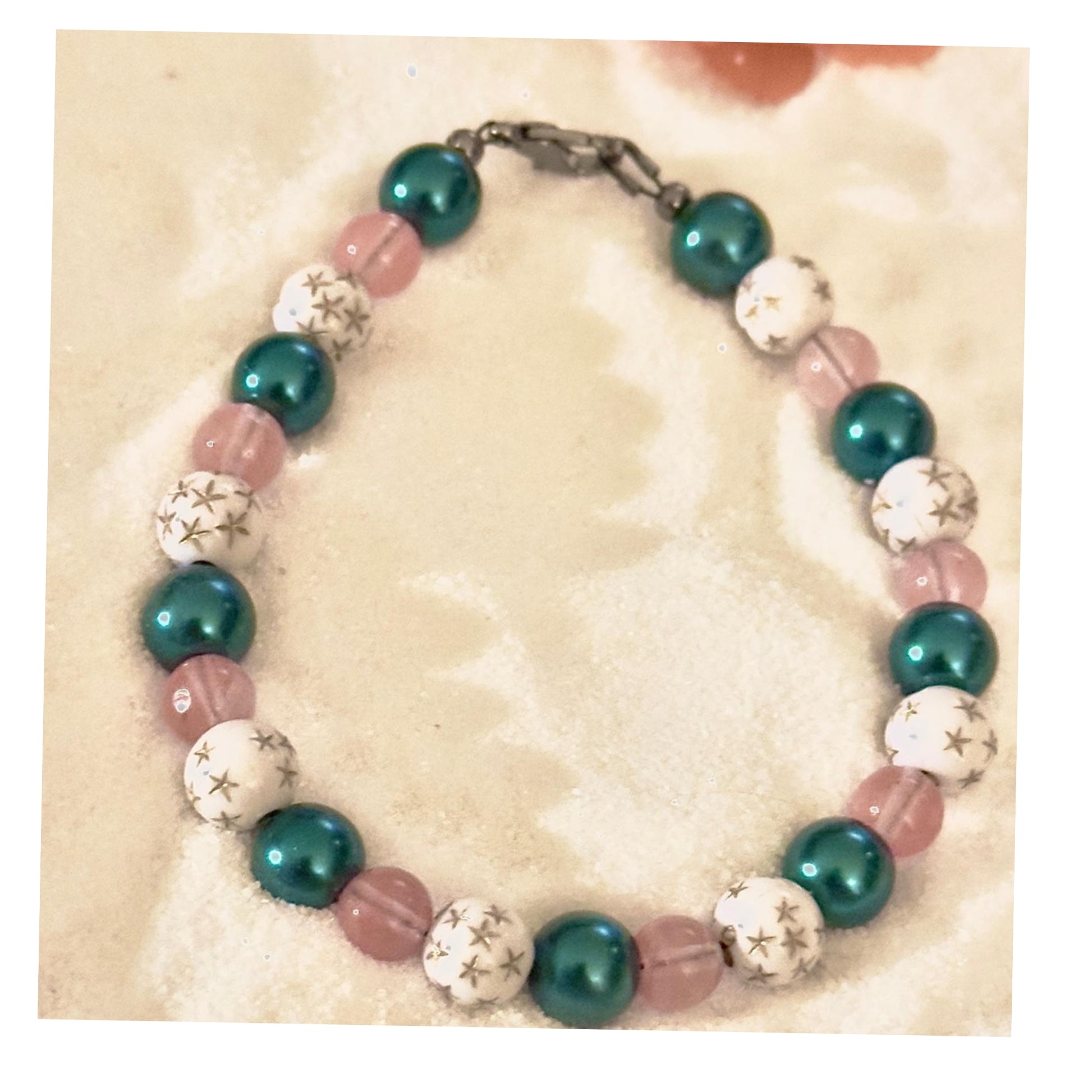 Handmade pink teal beaded bracelet with star accents on neutral sand background