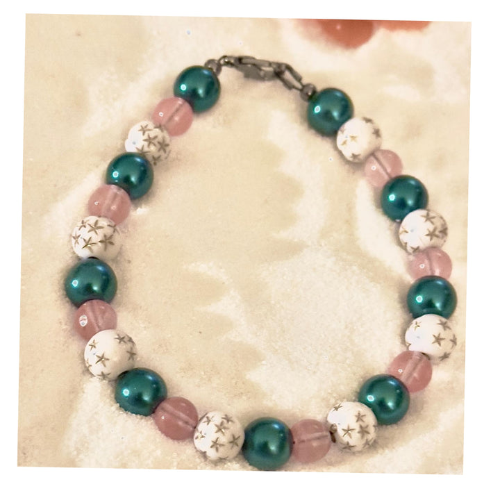Handmade pink teal beaded bracelet with star accents on neutral sand background