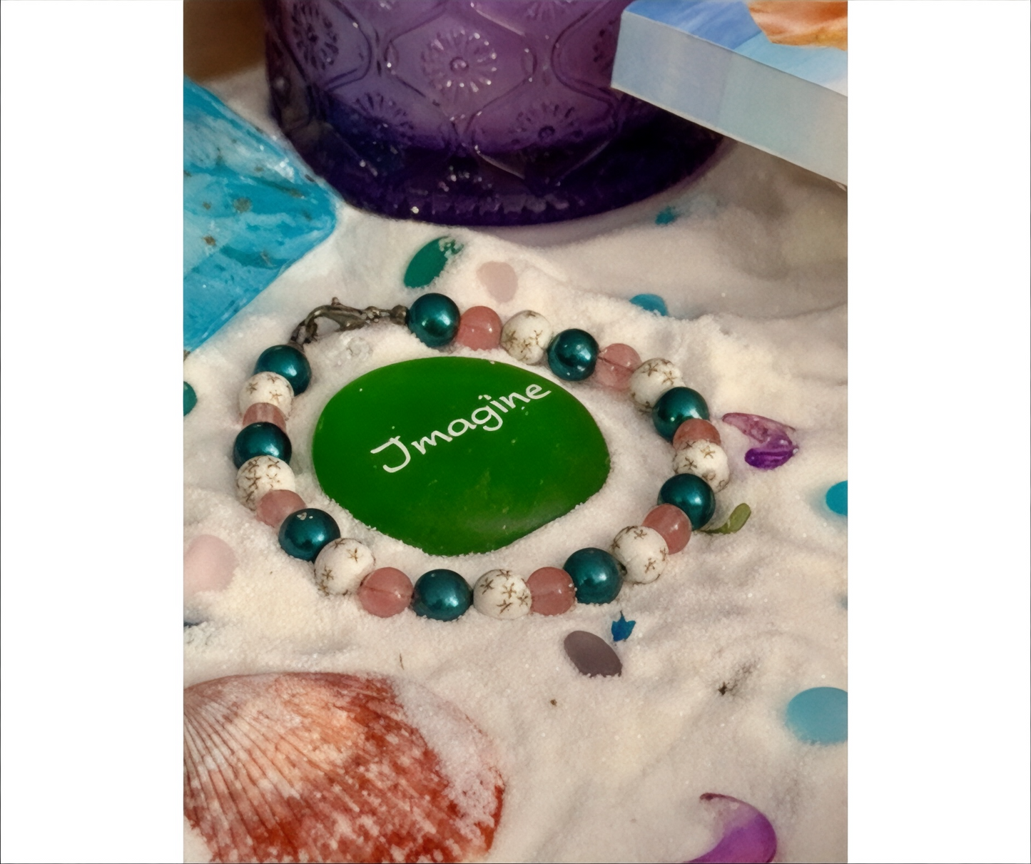 Galaxy beaded bracelet with pink teal beads styled on beach sand with shells