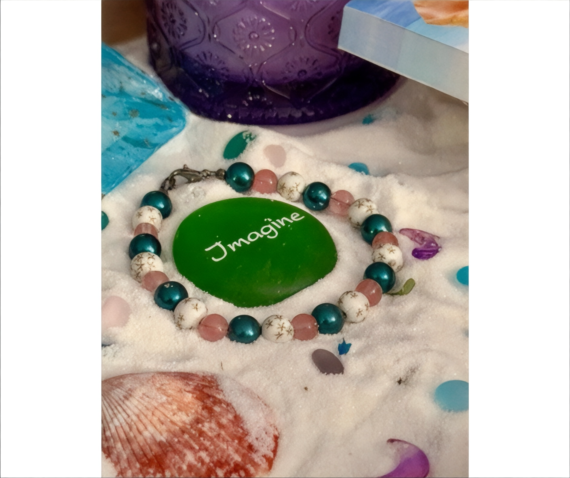 Galaxy beaded bracelet with pink teal beads styled on beach sand with shells
