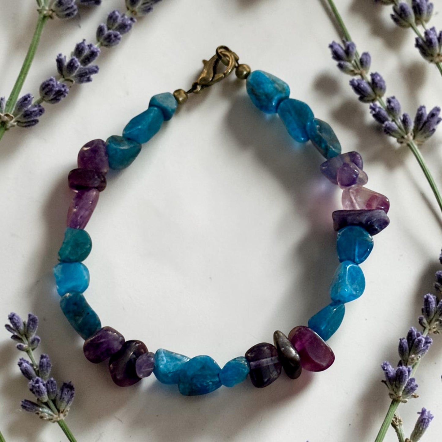     Handmade healing gemstone bracelet with Apatite and Amethyst stones surrounded by lavender sprigs on soft white background