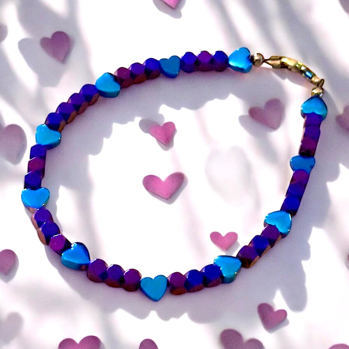 Heartspell Twilight bracelet surrounded by soft pink hearts, highlighting its romantic purple, blue, and turquoise color palette.