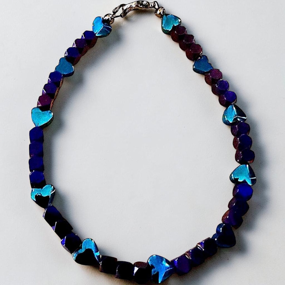 Heartspell Twilight bracelet featuring deep purple and blue beads with shimmering turquoise heart accents on a clean white background.