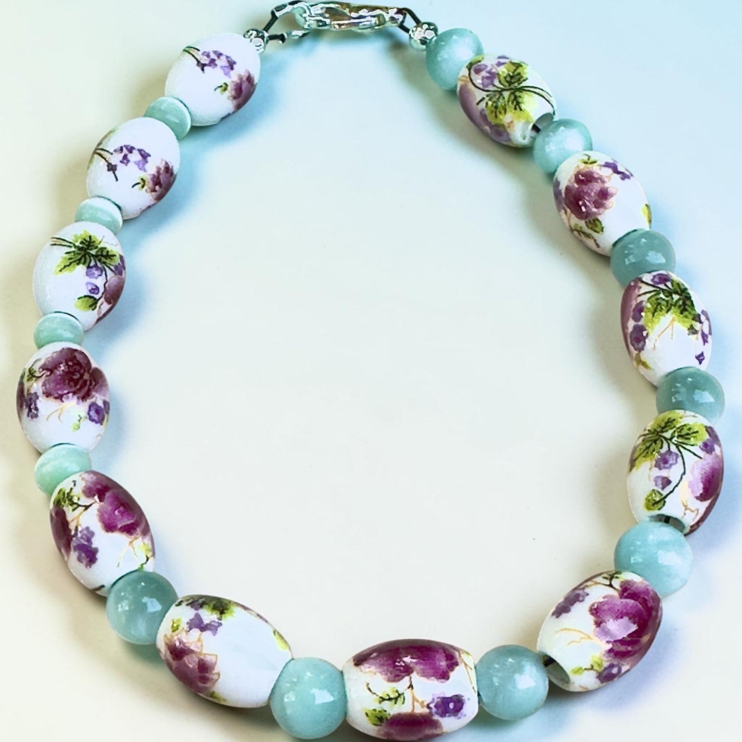Hidden Reverie Meadow bracelet featuring floral porcelain beads with pink and purple wildflower designs and soft aqua accent beads.