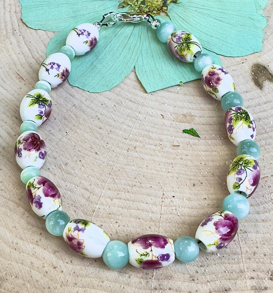 Nature-inspired floral bracelet displayed on a wood slice with pastel meadow colors and porcelain flower beads.