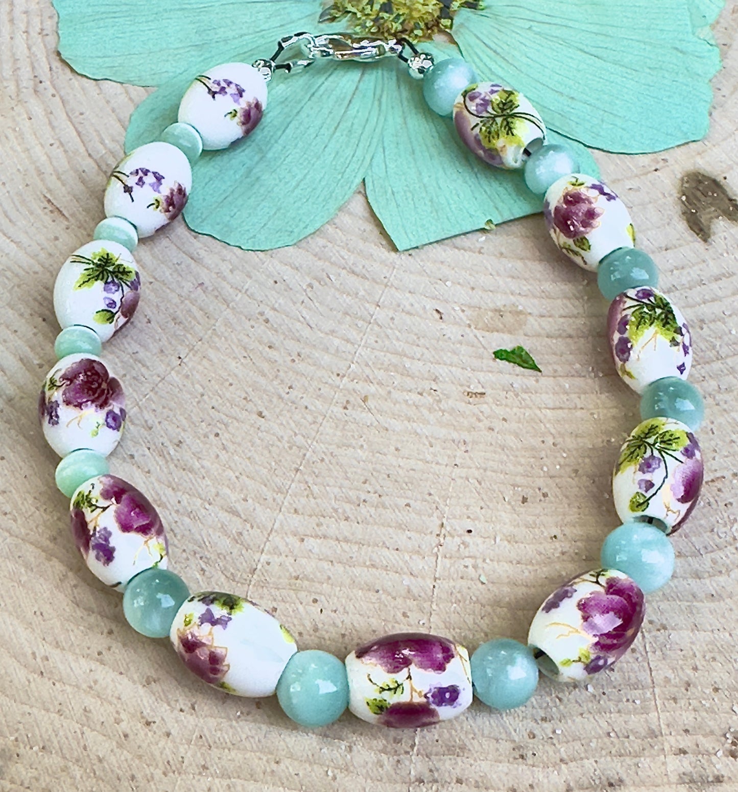 Nature-inspired floral bracelet displayed on a wood slice with pastel meadow colors and porcelain flower beads.