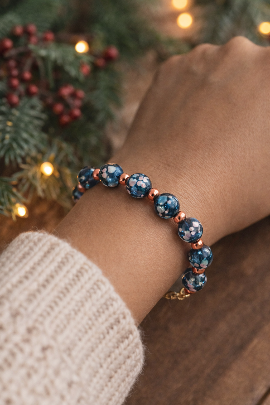 Celestial beaded bracelet worn on a wrist, showing blue galaxy-style glass beads and copper accents in warm winter lighting.