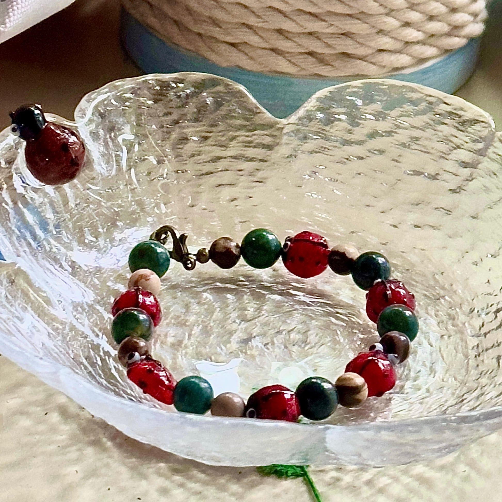 Ladybug bracelet displayed inside a textured glass bowl with warm natural lighting.