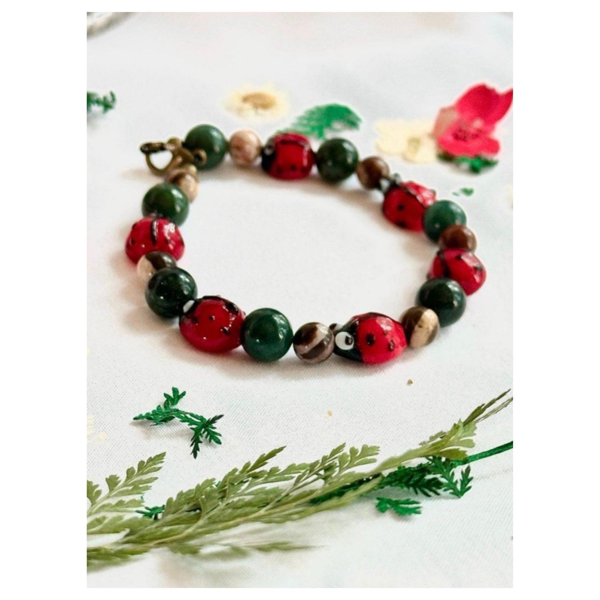 Whimsical ladybug bracelet styled with greenery and floral accents on soft white fabric.