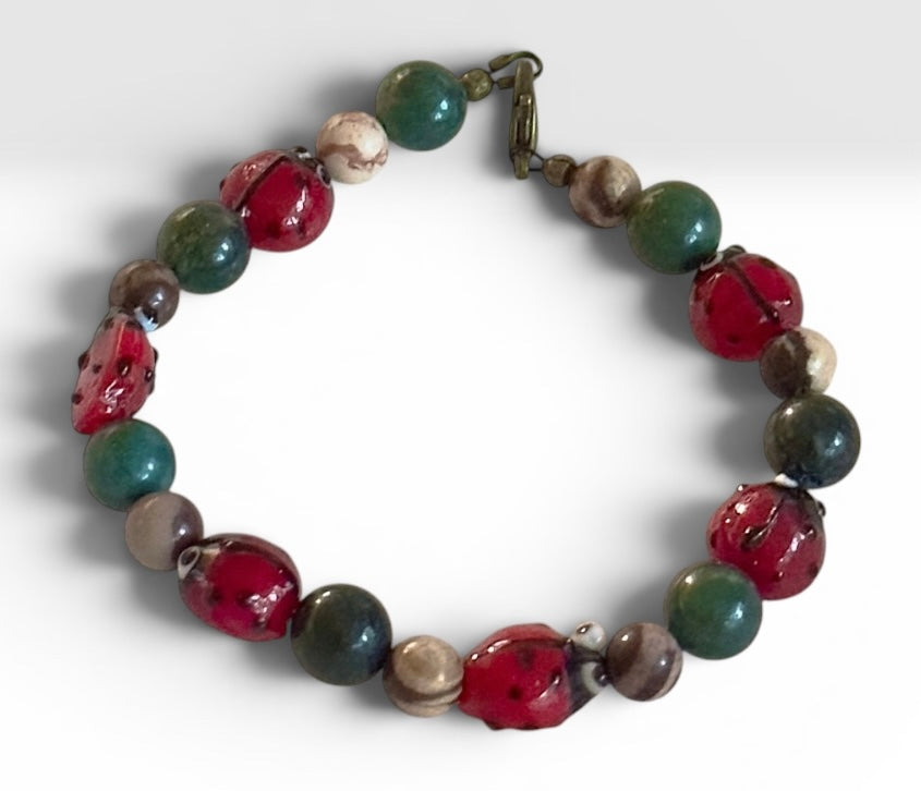 Handmade ladybug bracelet featuring red ladybug beads, green jade beads, and Brown Zebra Jasper on a white background.