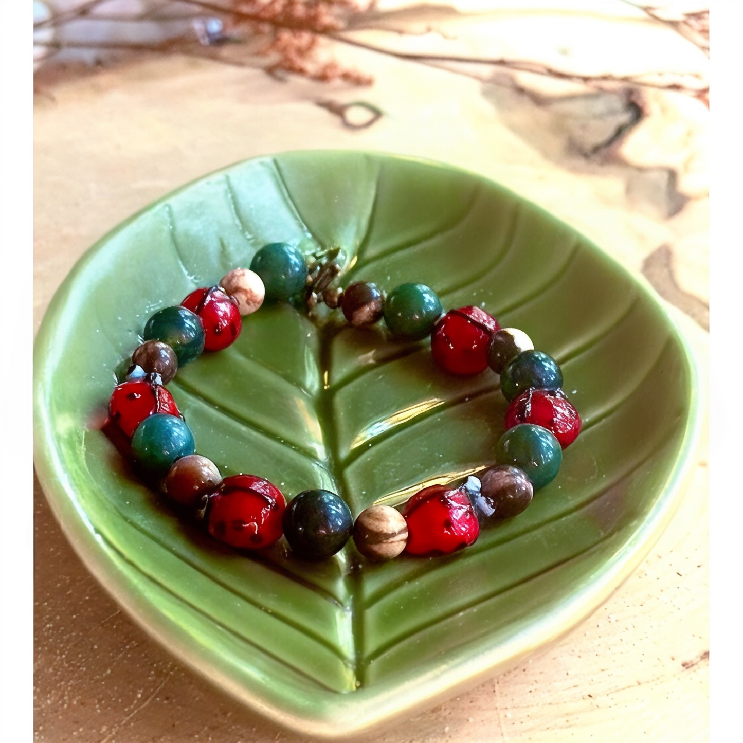 Nature-inspired ladybug bracelet styled on a green ceramic leaf dish in sunlight.
