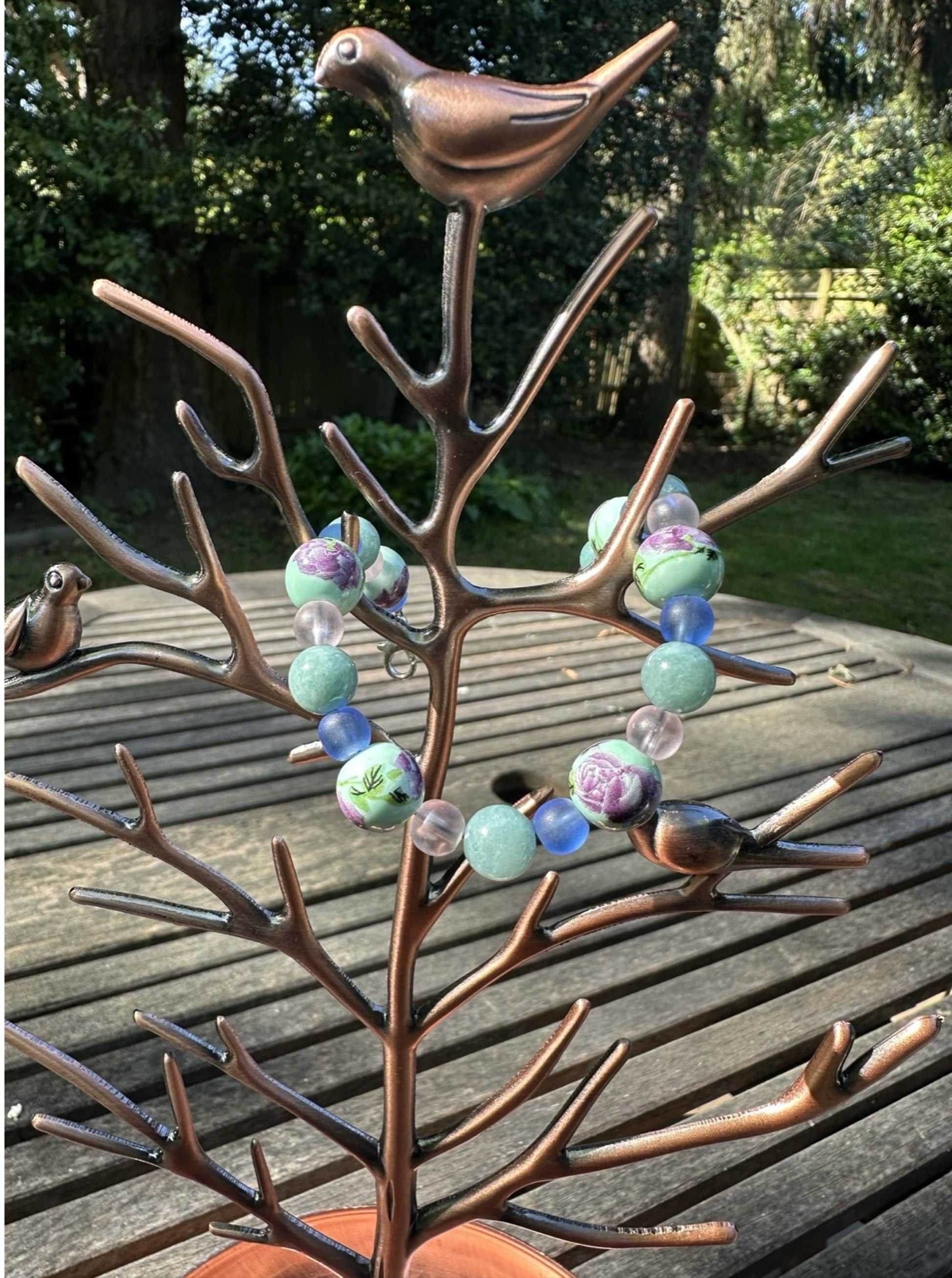 Handmade whimsical floral bracelet hanging on a rustic jewelry display outdoors in natural light