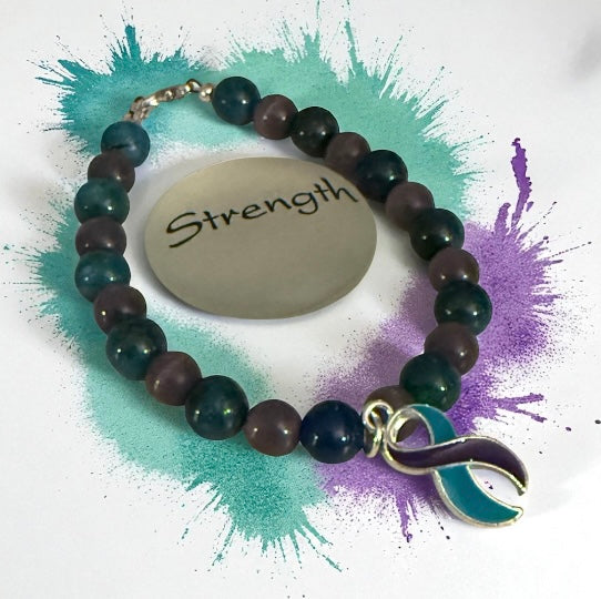 Gemstone awareness bracelet displayed beside a Strength inspiration stone with teal and purple accents.