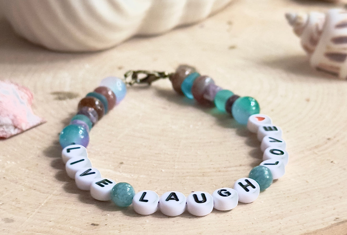 Bracelet with 'LIVE LAUGH LOVE' beads on a wooden surface and shells