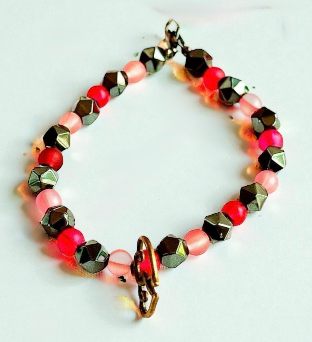 Soul Connection handmade beaded bracelet featuring pink, raspberry, hematite, and black beads with an intertwined heart charm on a white background.