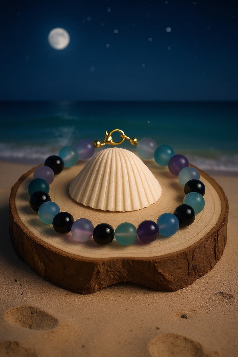 Lunar Twilight Galaxy gemstone bracelet displayed on a wood slice with a seashell under a moonlit beach sky, creating a peaceful celestial coastal scene.