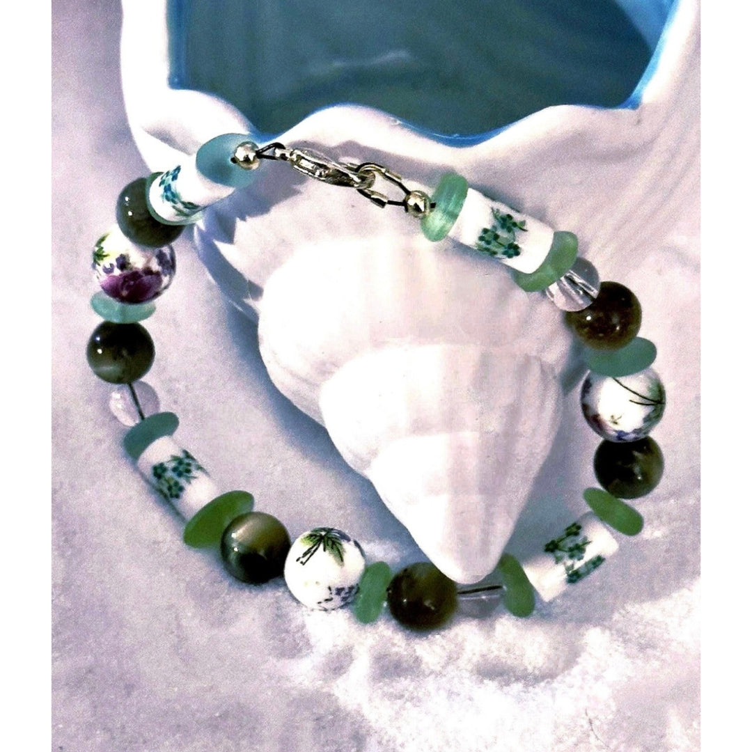 Close-up of the Meadowlight bracelet styled around a pale seashell, showing its green and floral beads.