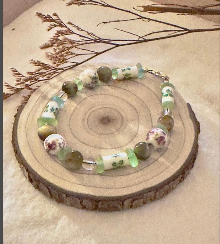 Close-up of the Meadowlight bracelet styled around a pale seashell, showing its green and floral beads.